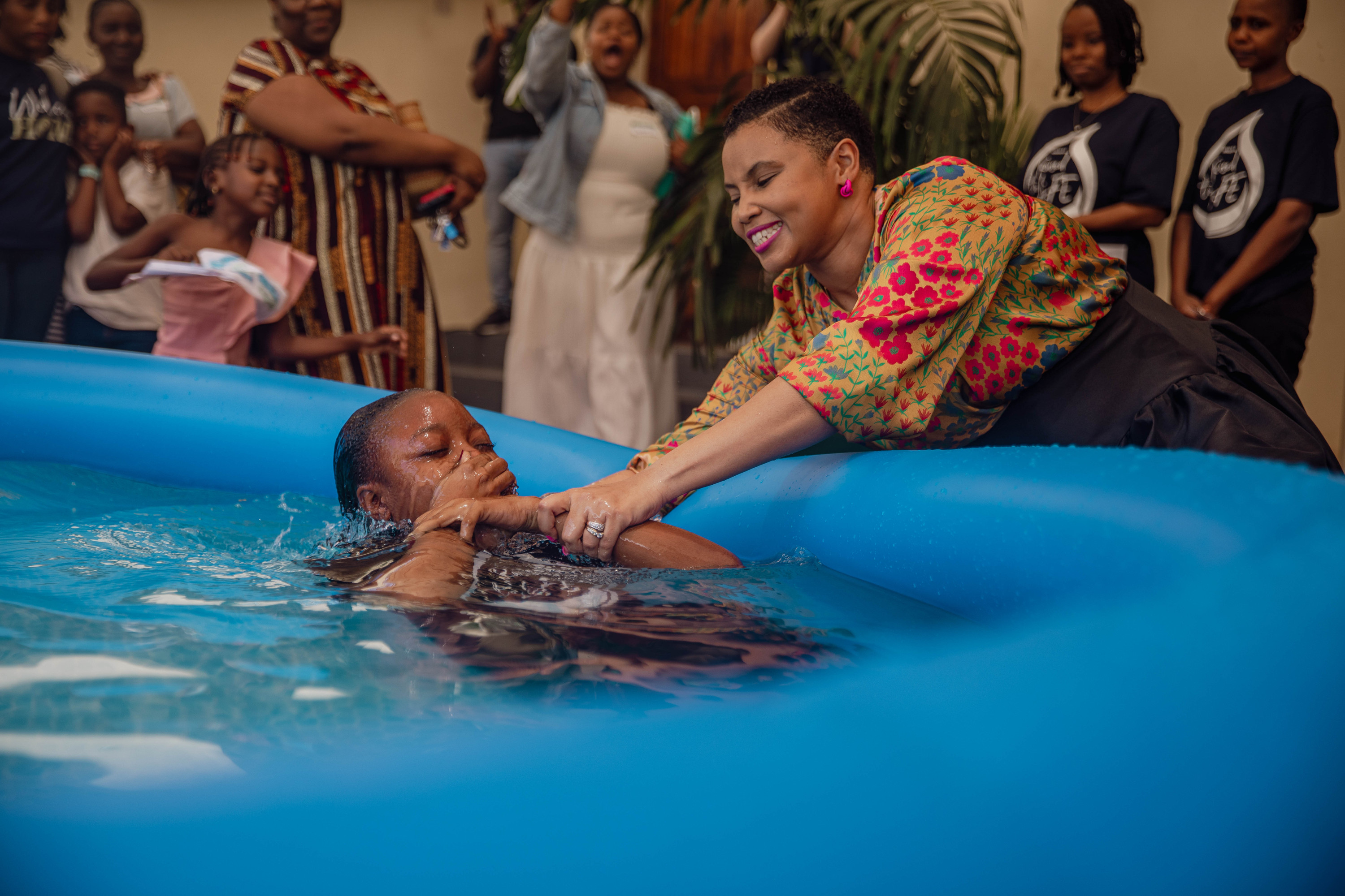 A leader baptises a woman in the pool while people cheer