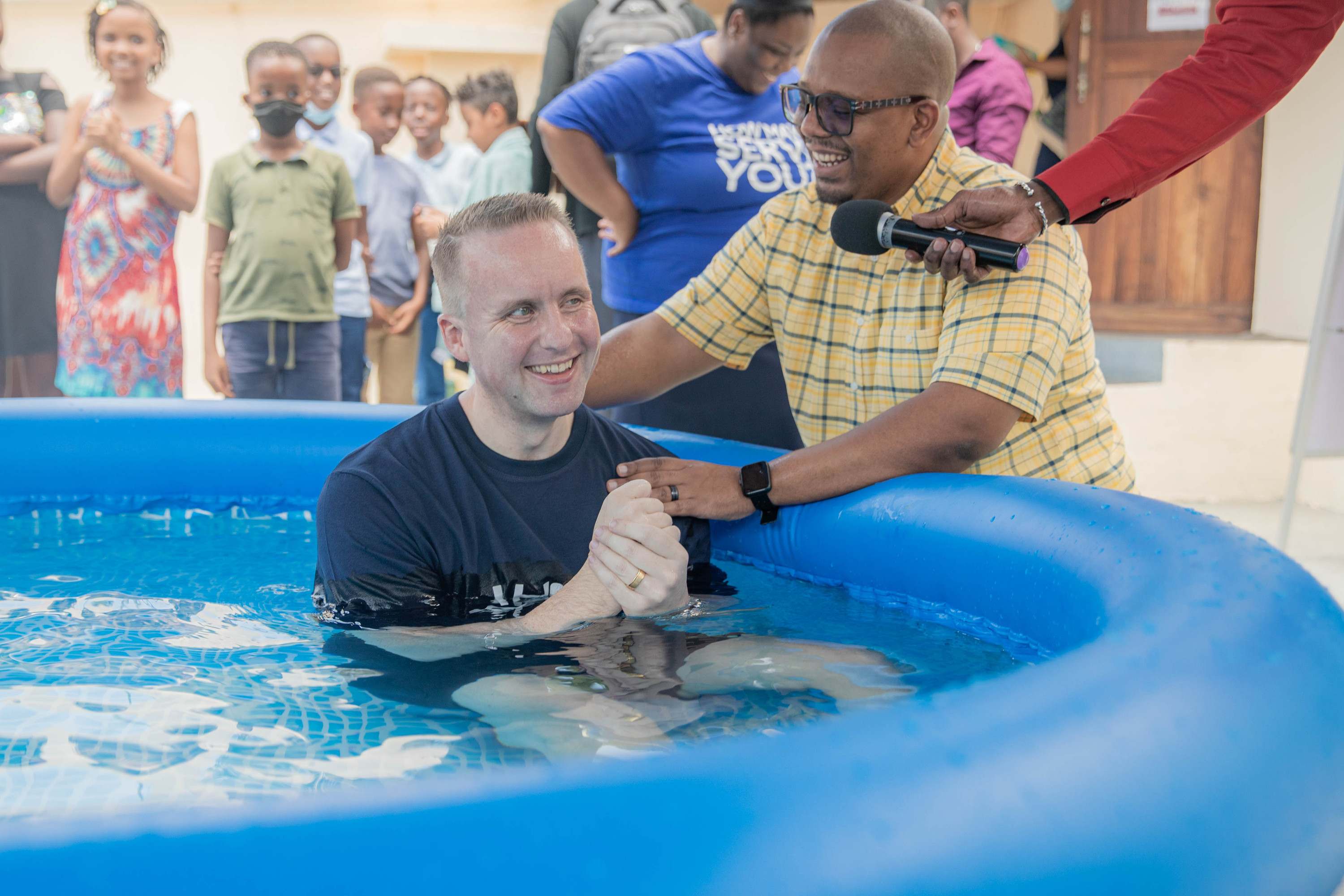 A man laughs in the baptism pool as a leader holds his hands