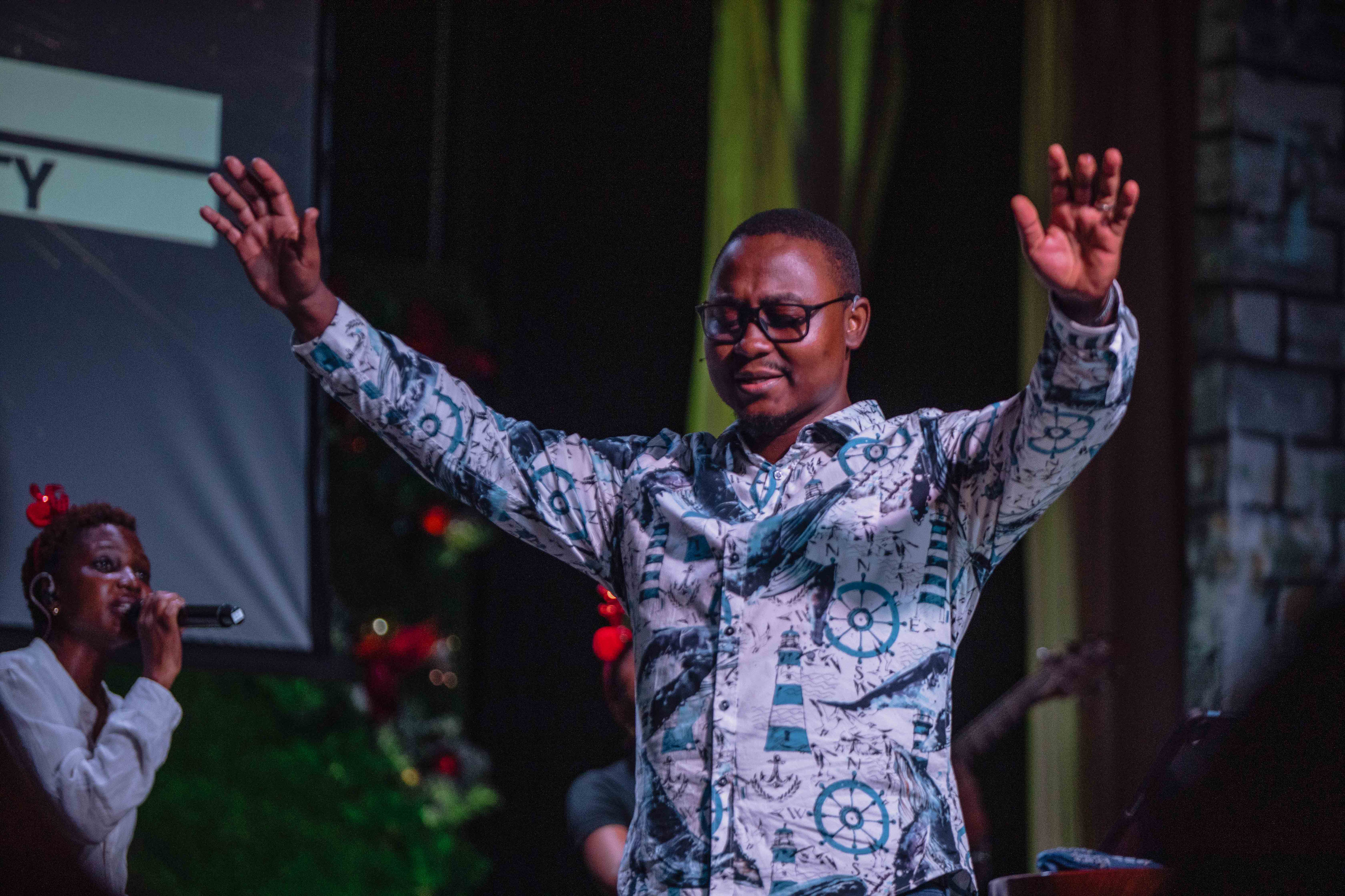 A preacher on stage opens his arms wide