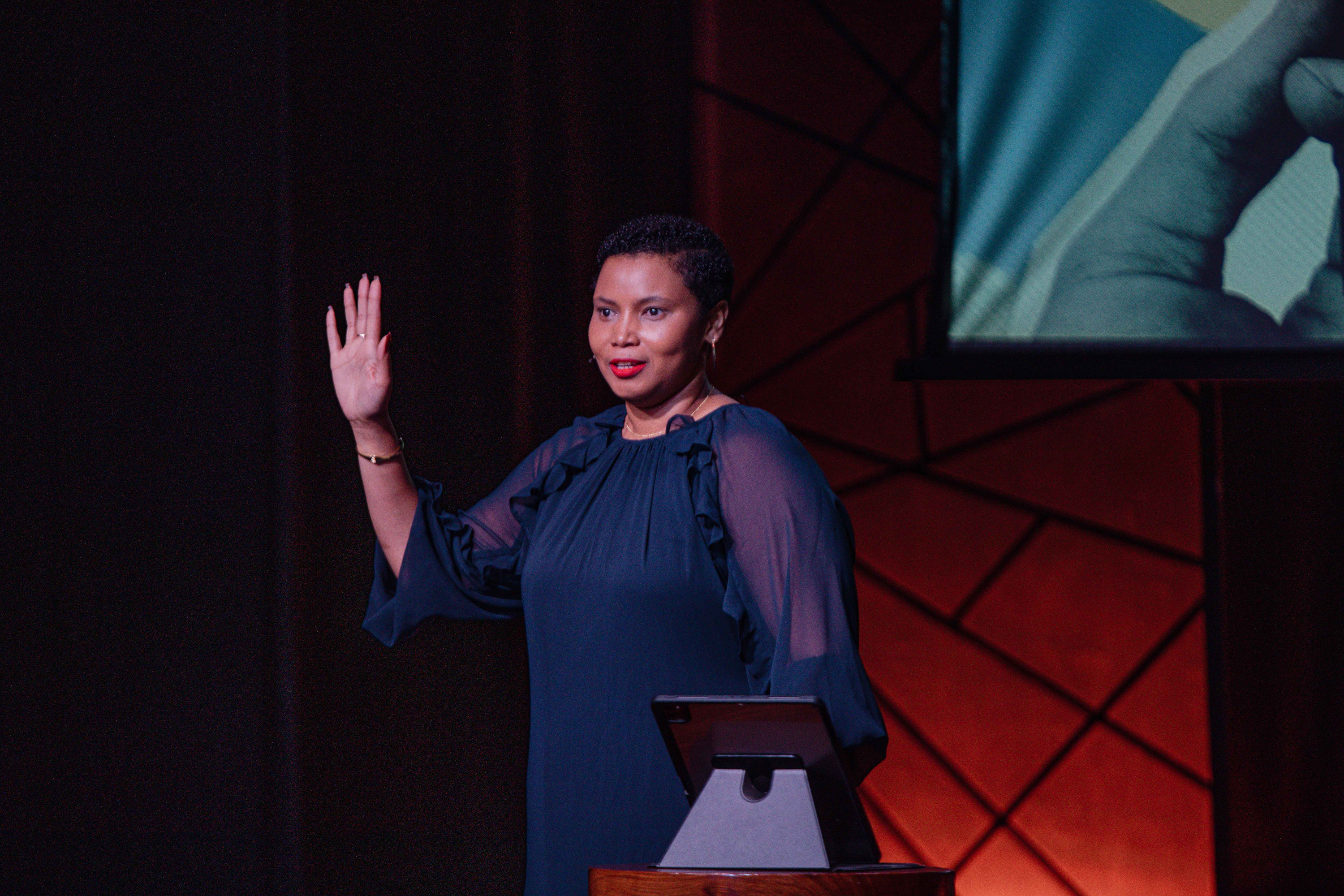 A woman speaks from the stage with one hand raised