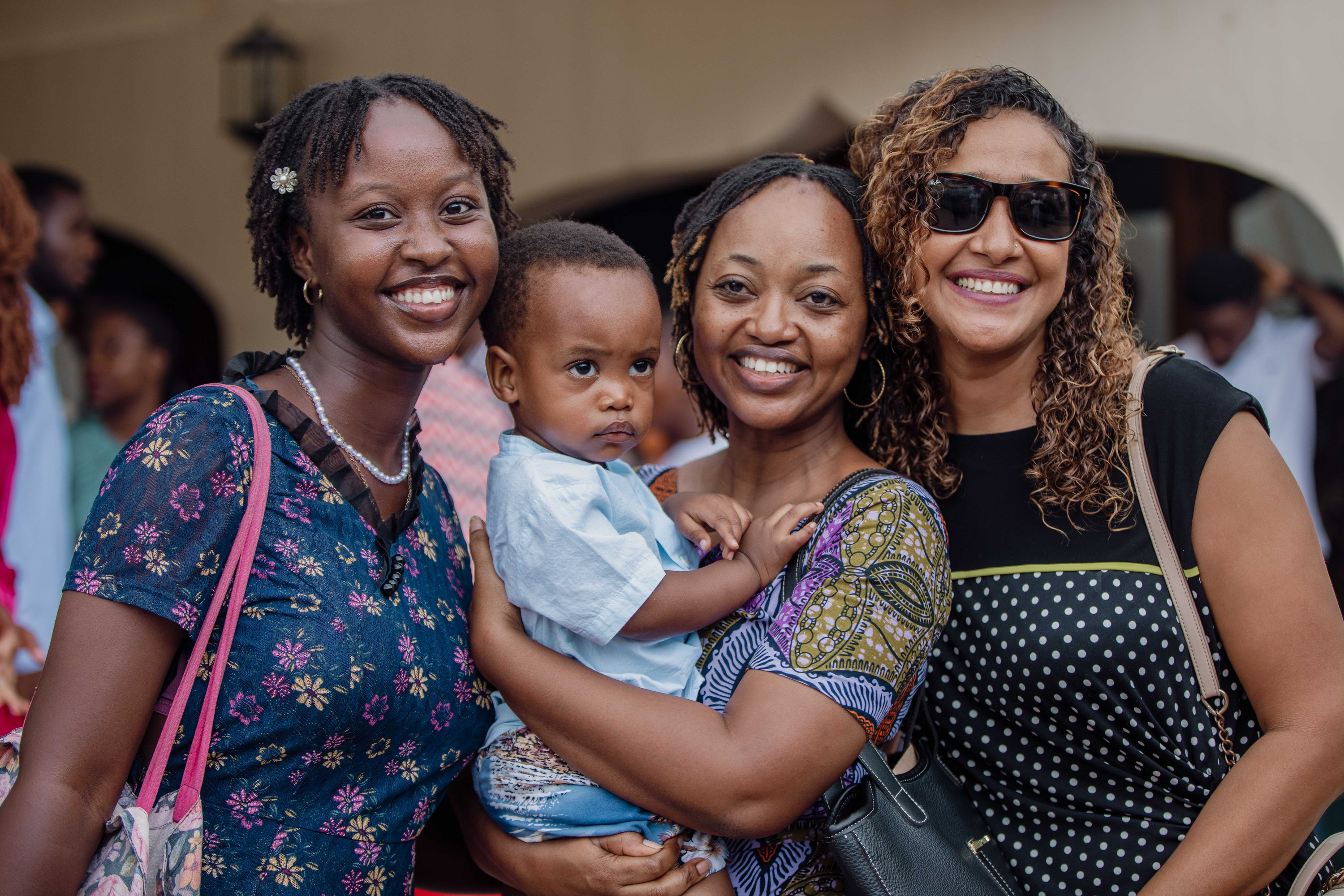 Three women smile together, one holding a toddler