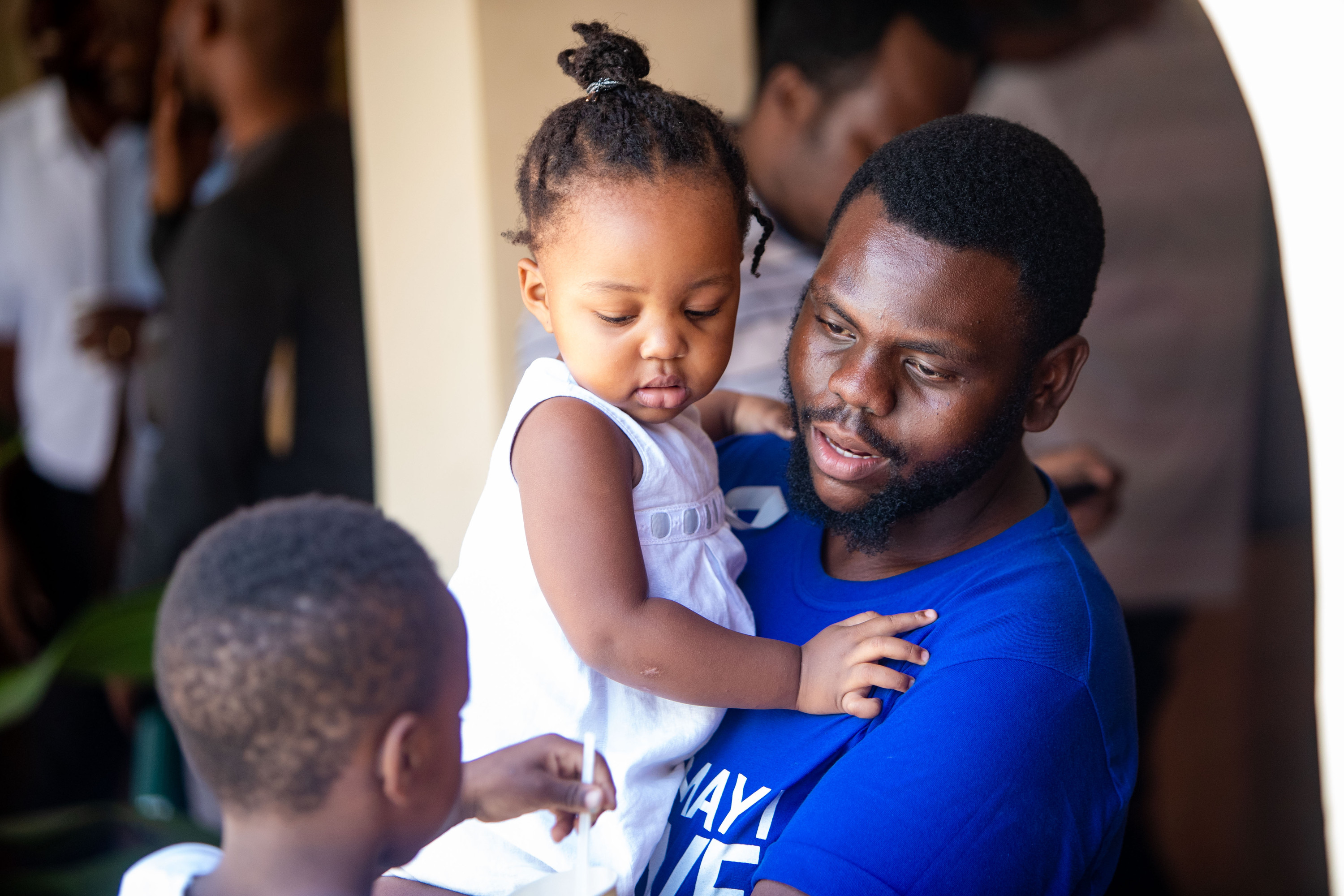 A father holds his toddler daughter, his son beside them