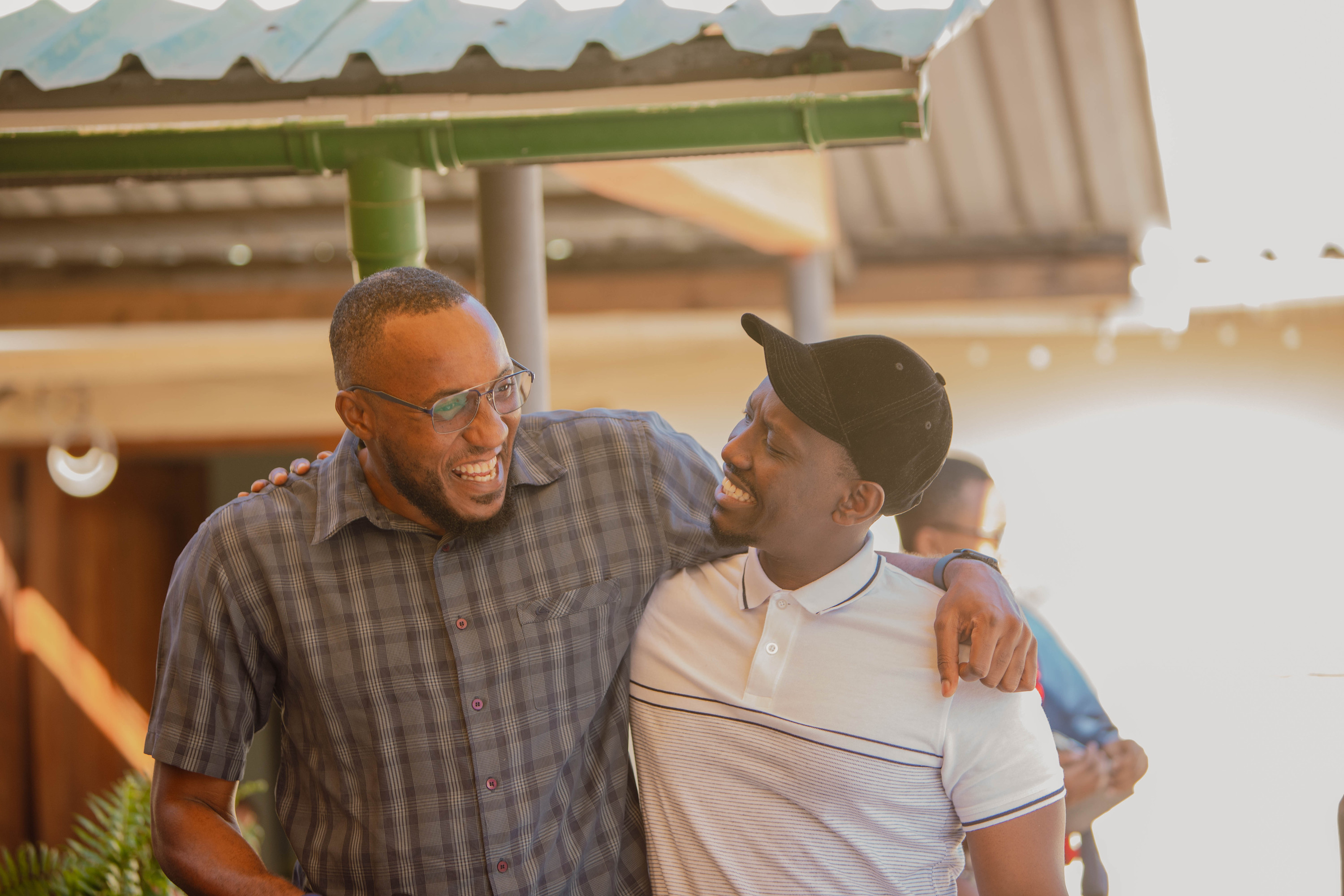Two men laugh together, one with his arm around the other