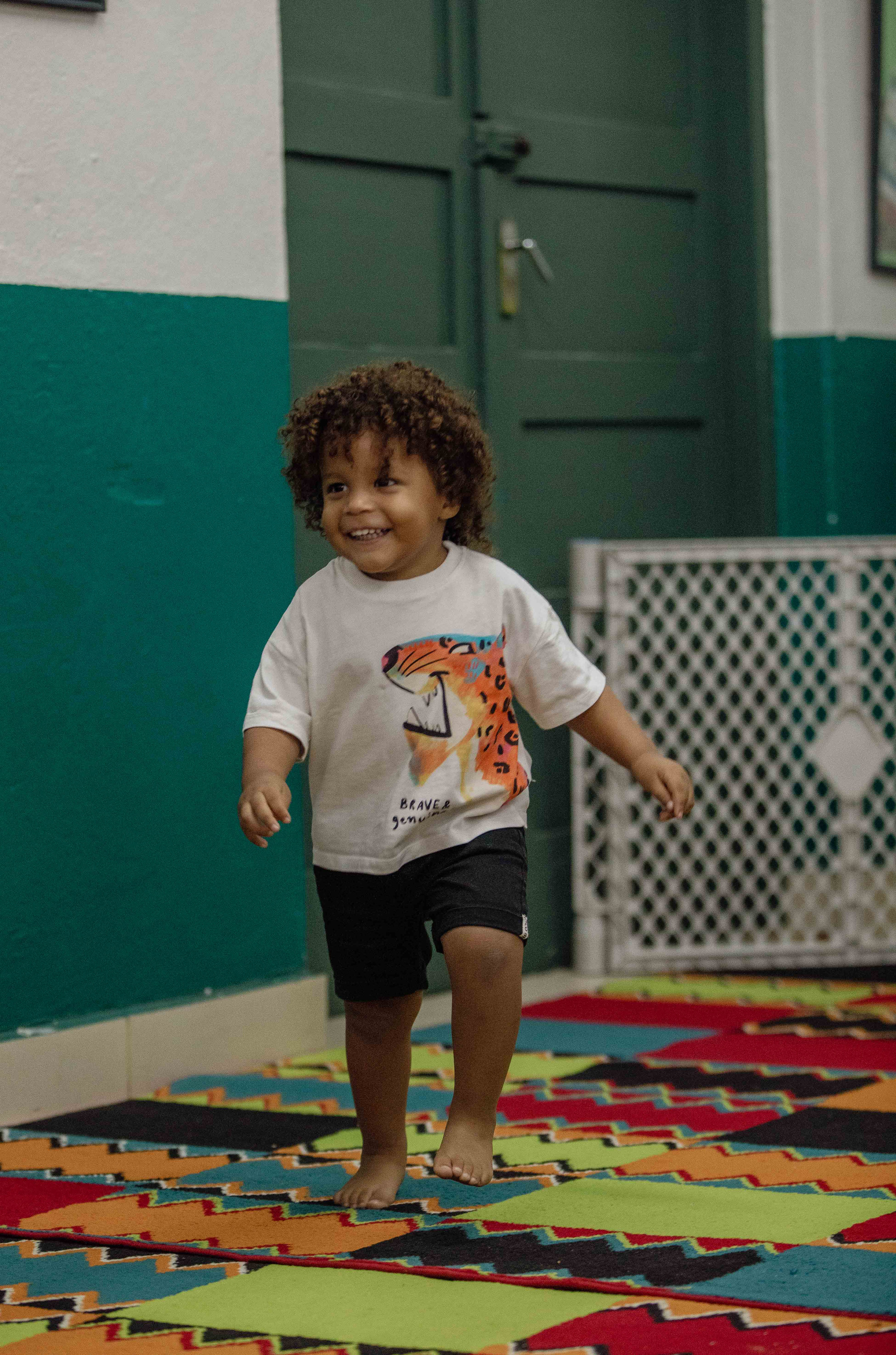 A toddler stands on a colourful rug