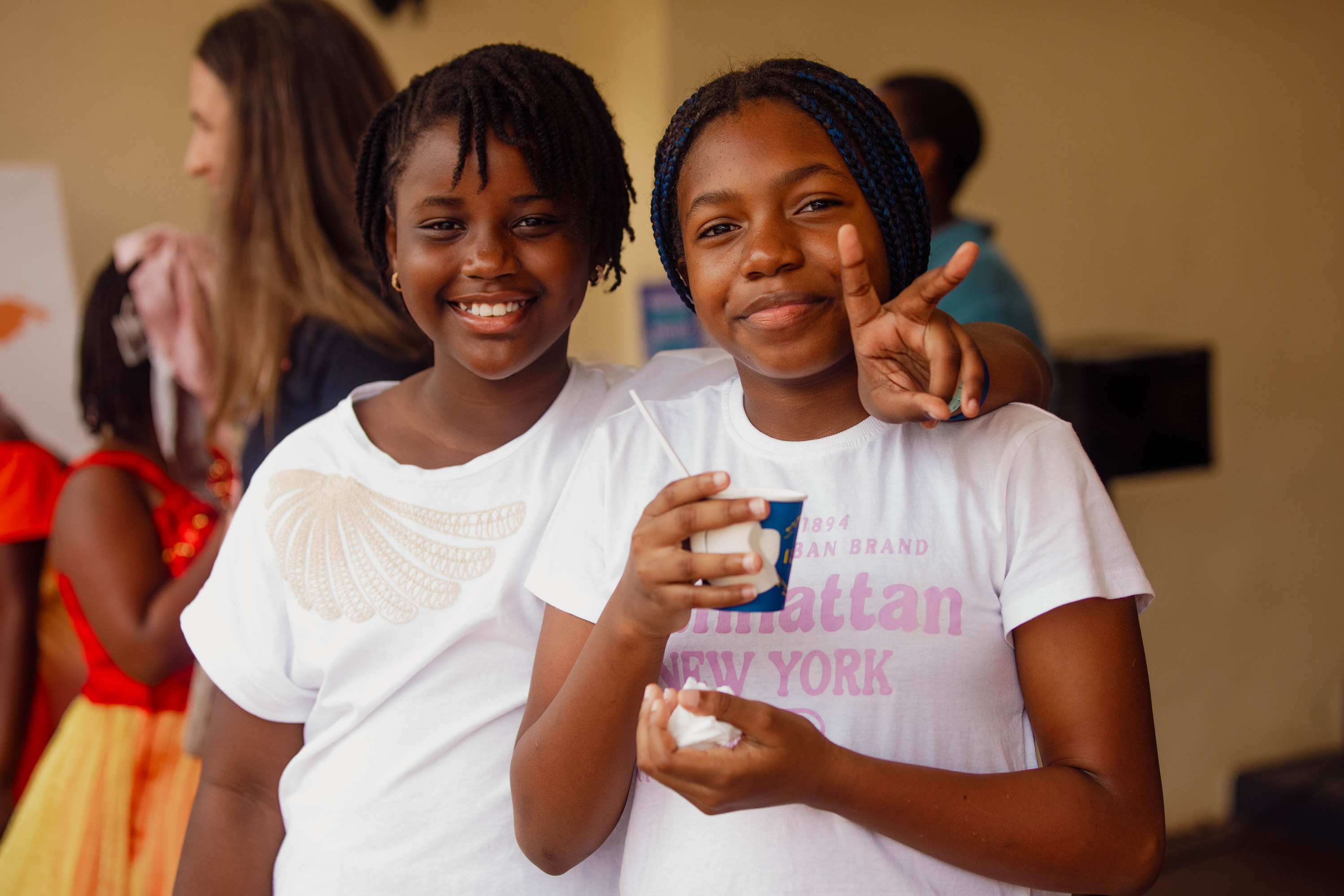 Two pre-teen girls smile, one making a peace sign