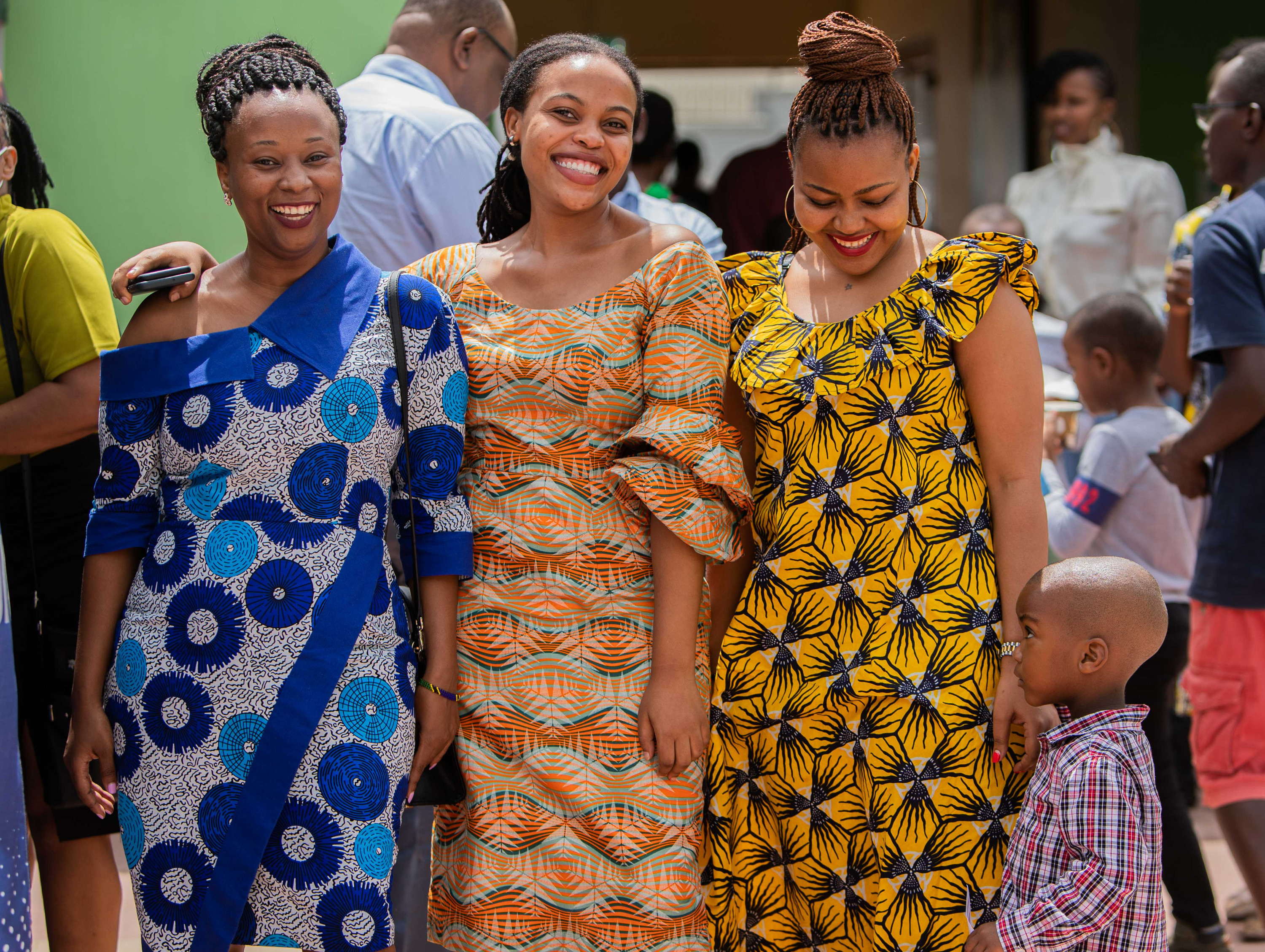 Three women in bright African-print dresses smile together