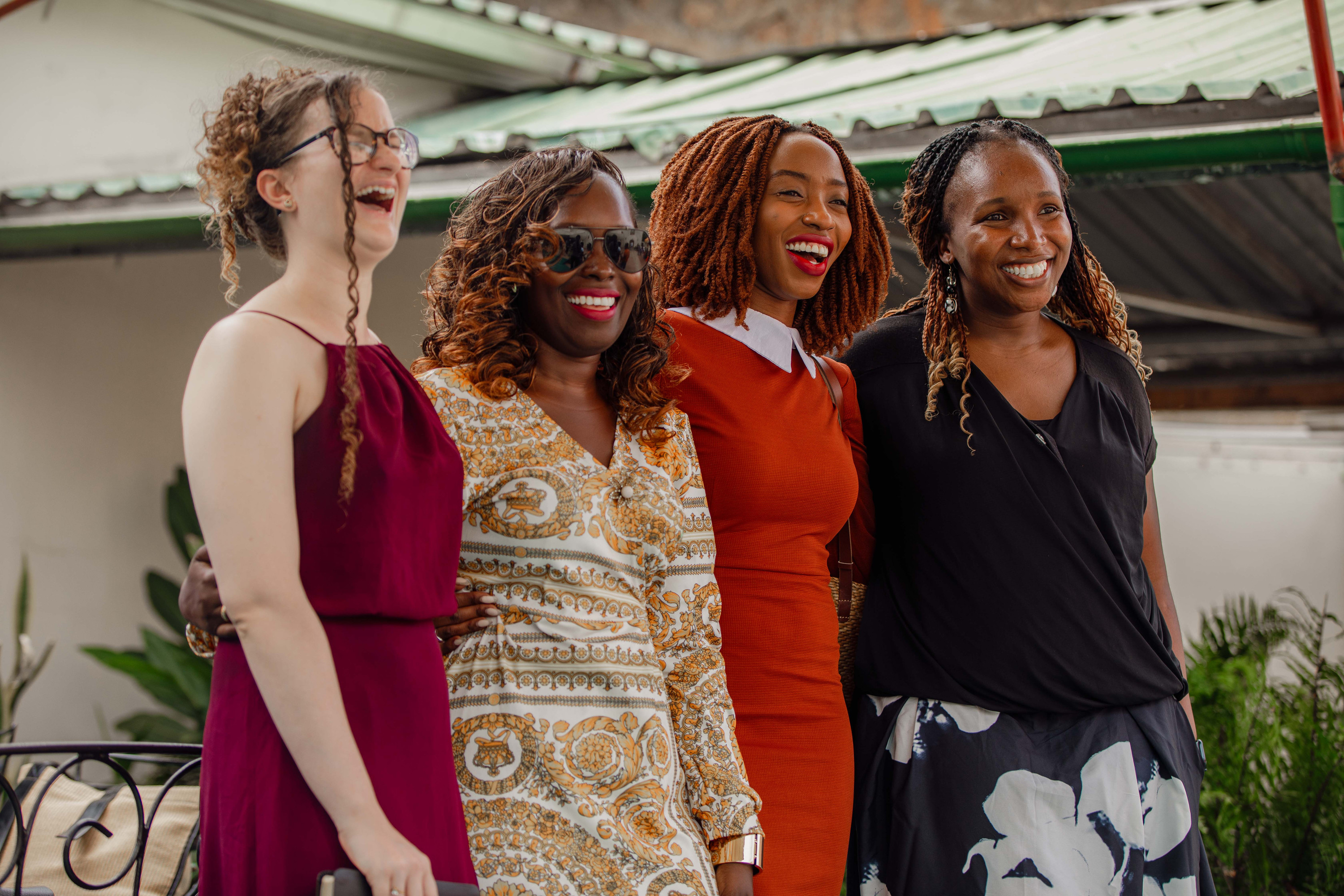 Four women stand together, laughing