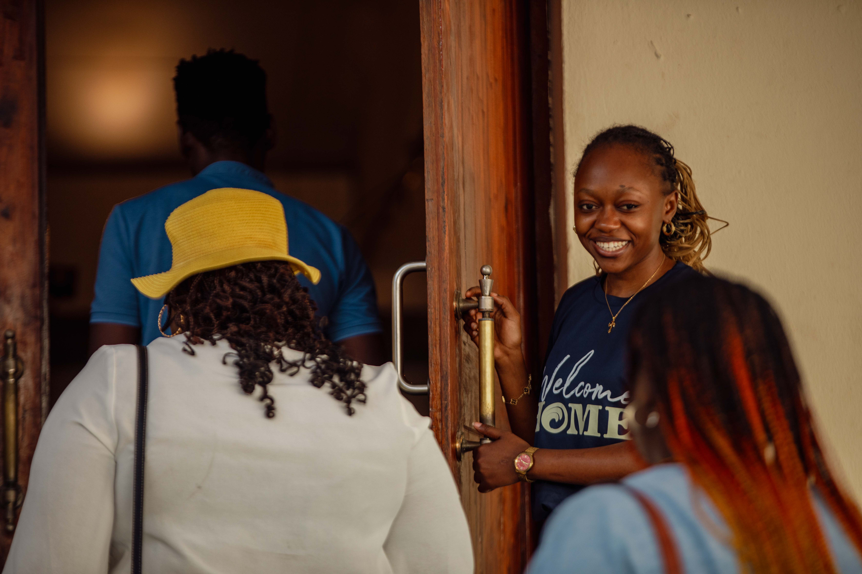 A volunteer in a Welcome Home T-shirt holds the door open as people arrive