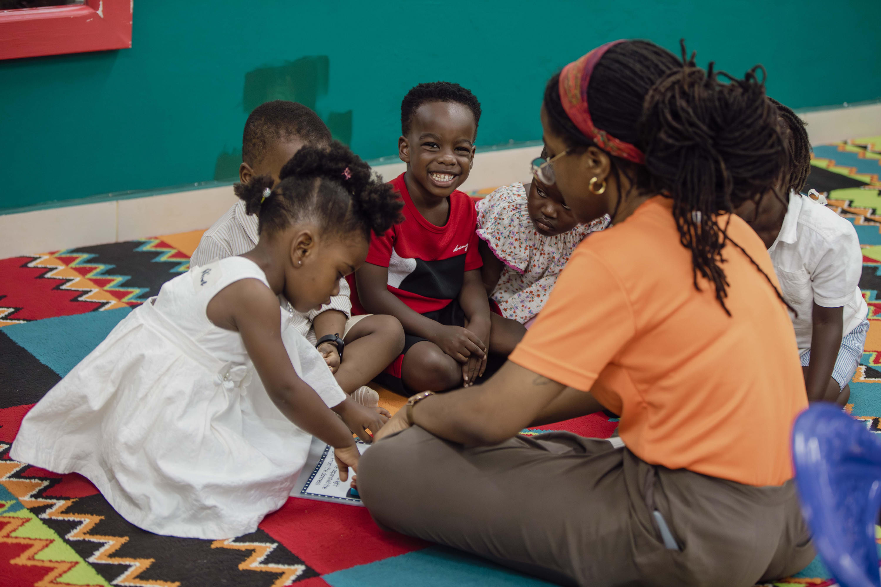 A volunteer sits on the play mat with toddlers around her