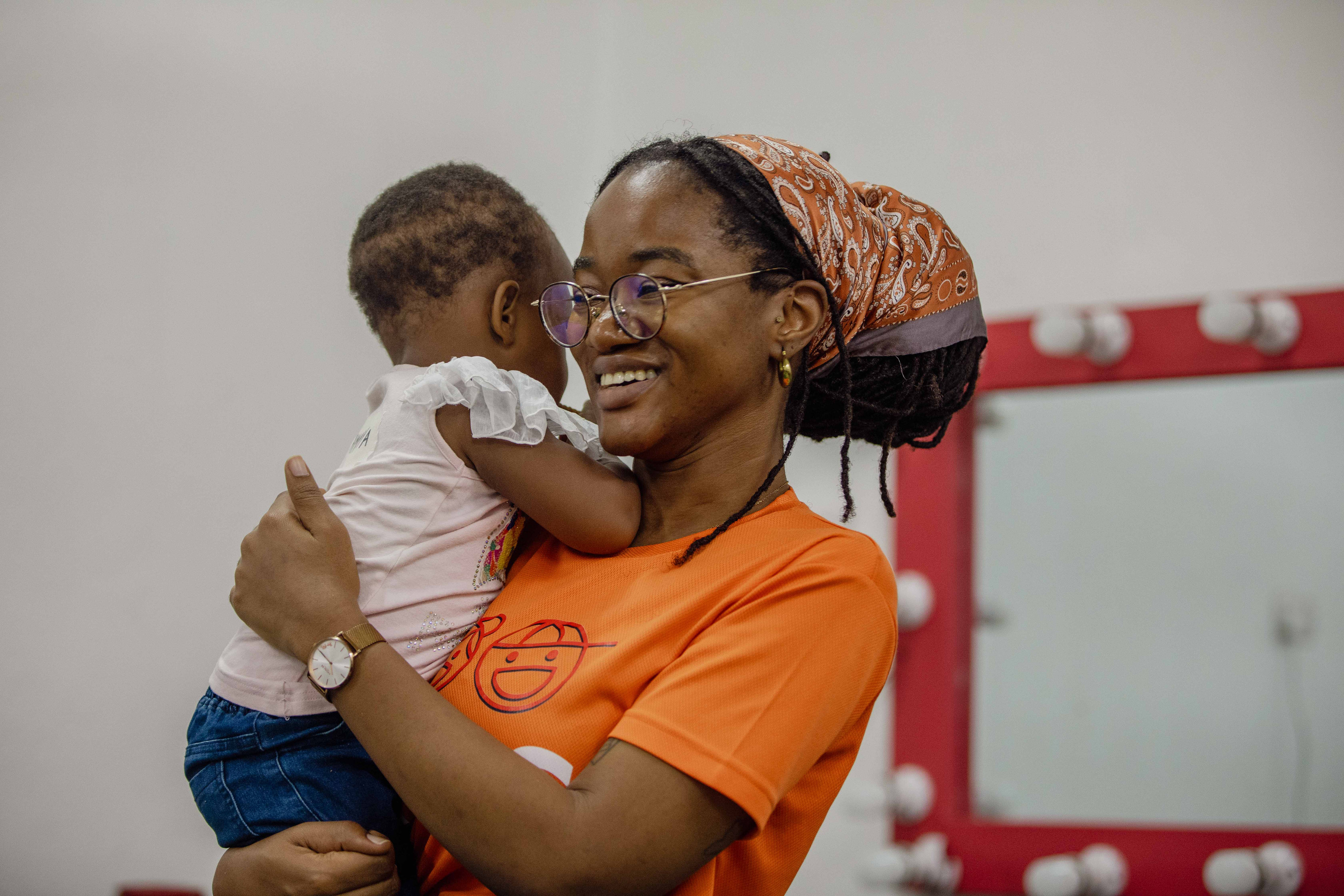 A volunteer in a KIDS T-shirt holds a baby and laughs