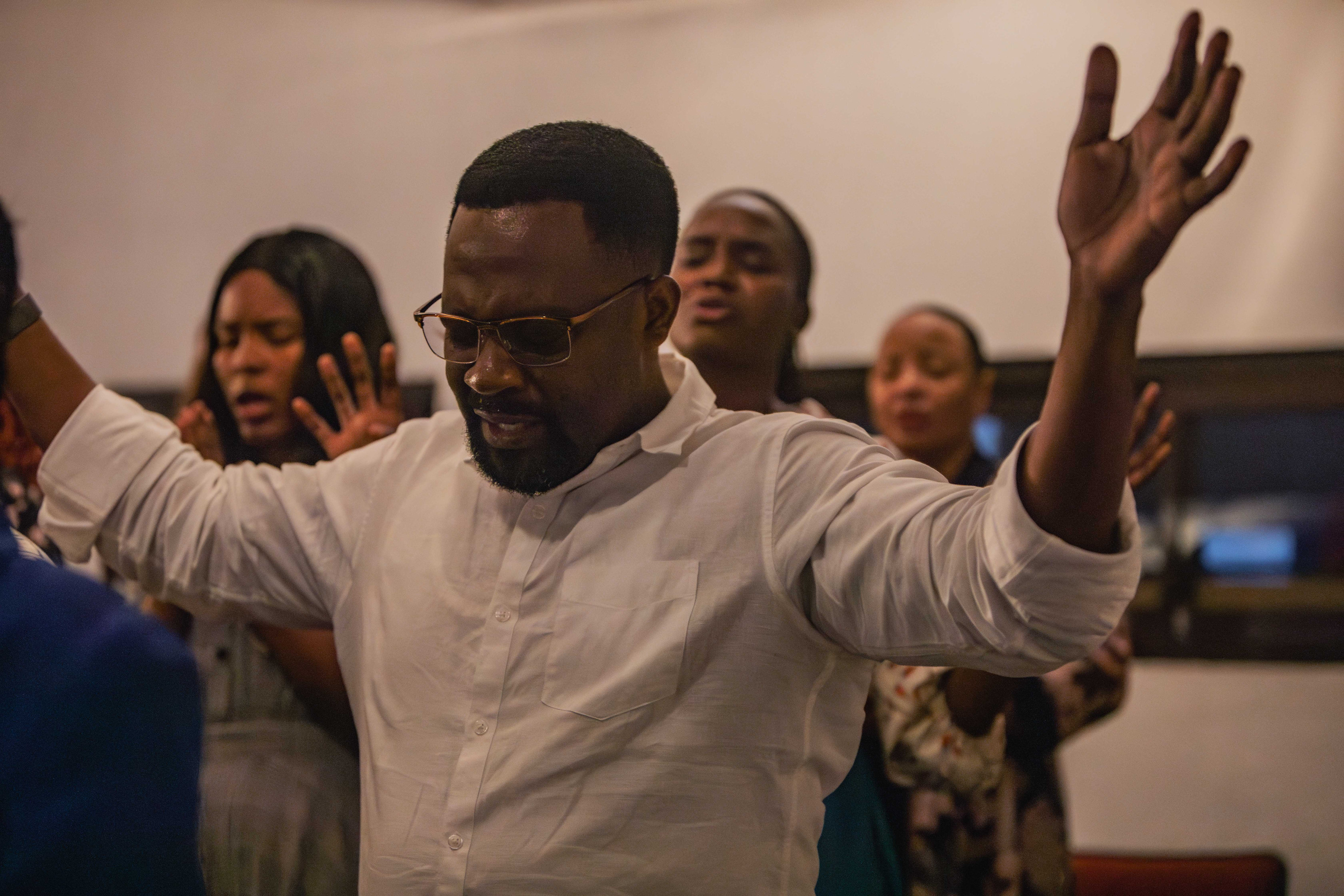A man lifts both arms in worship as people sing behind him