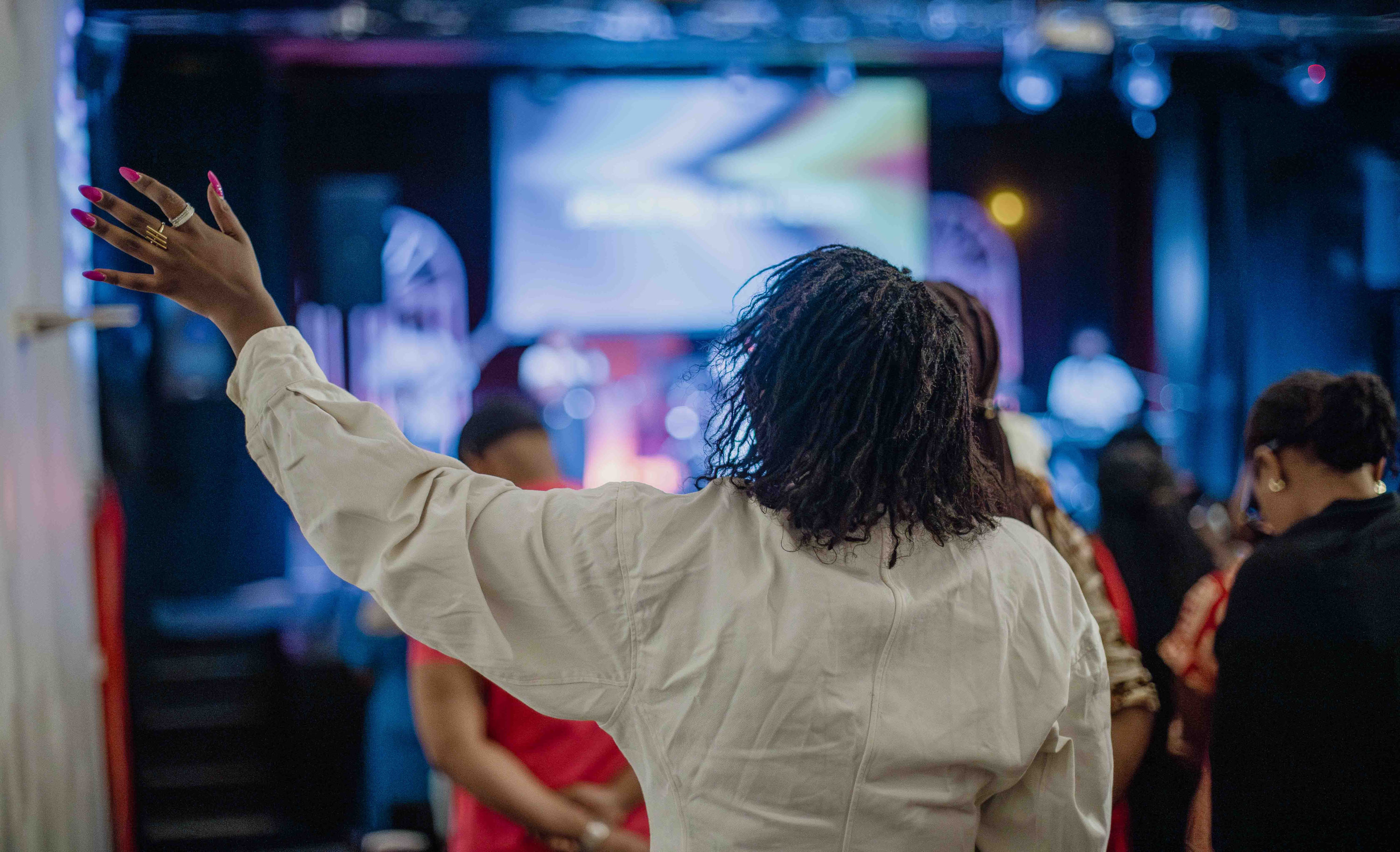 Seen from behind, a woman in white raises her hand towards the stage
